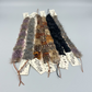 A collection of handmade feather hat band accessories including ostrich feathers, spotted duck feathers, and dark iridescent feathers. These bands come with a strap.